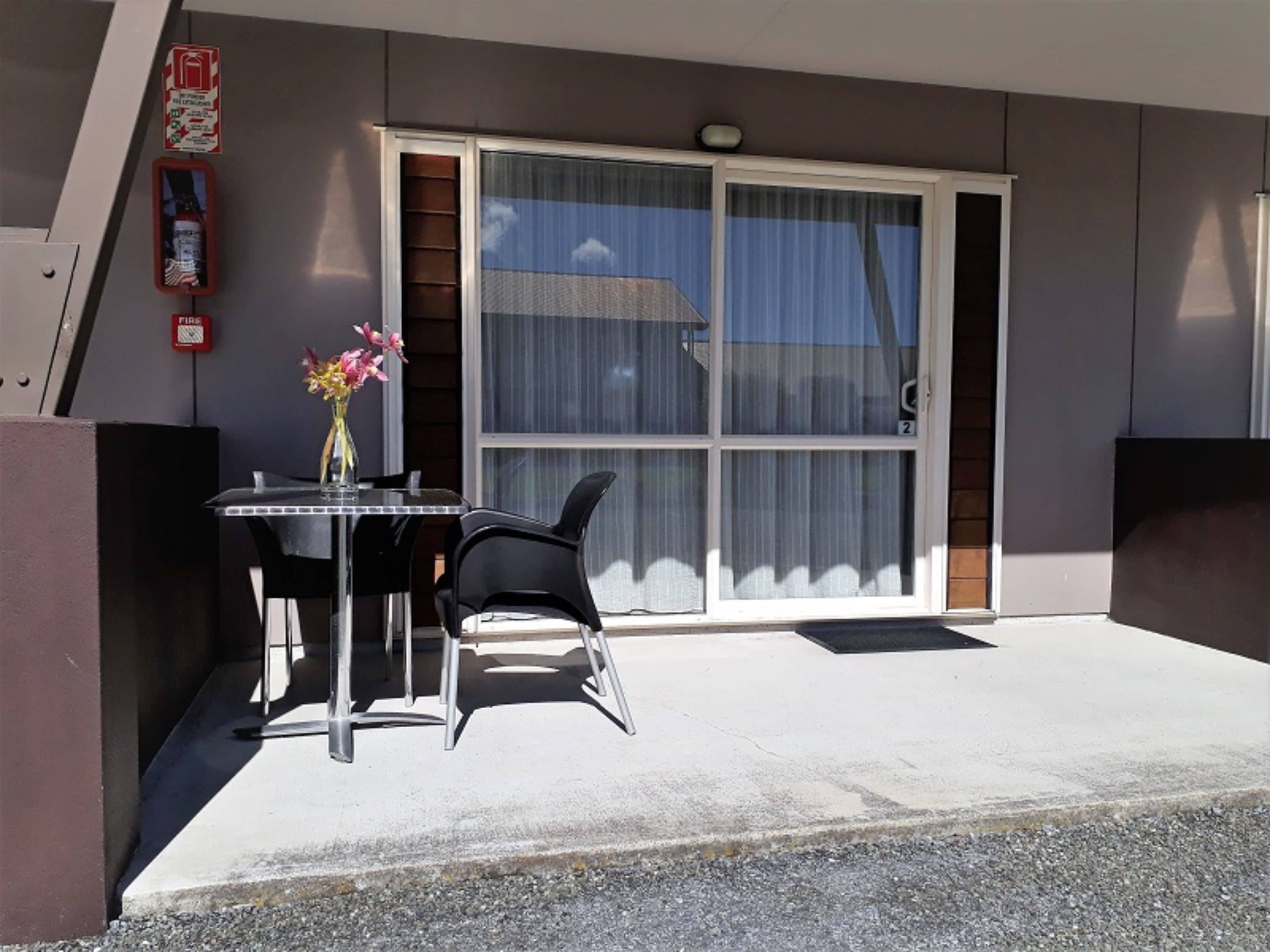 A modern building with a large sliding glass door, a small table with chairs, and a vase with flowers.