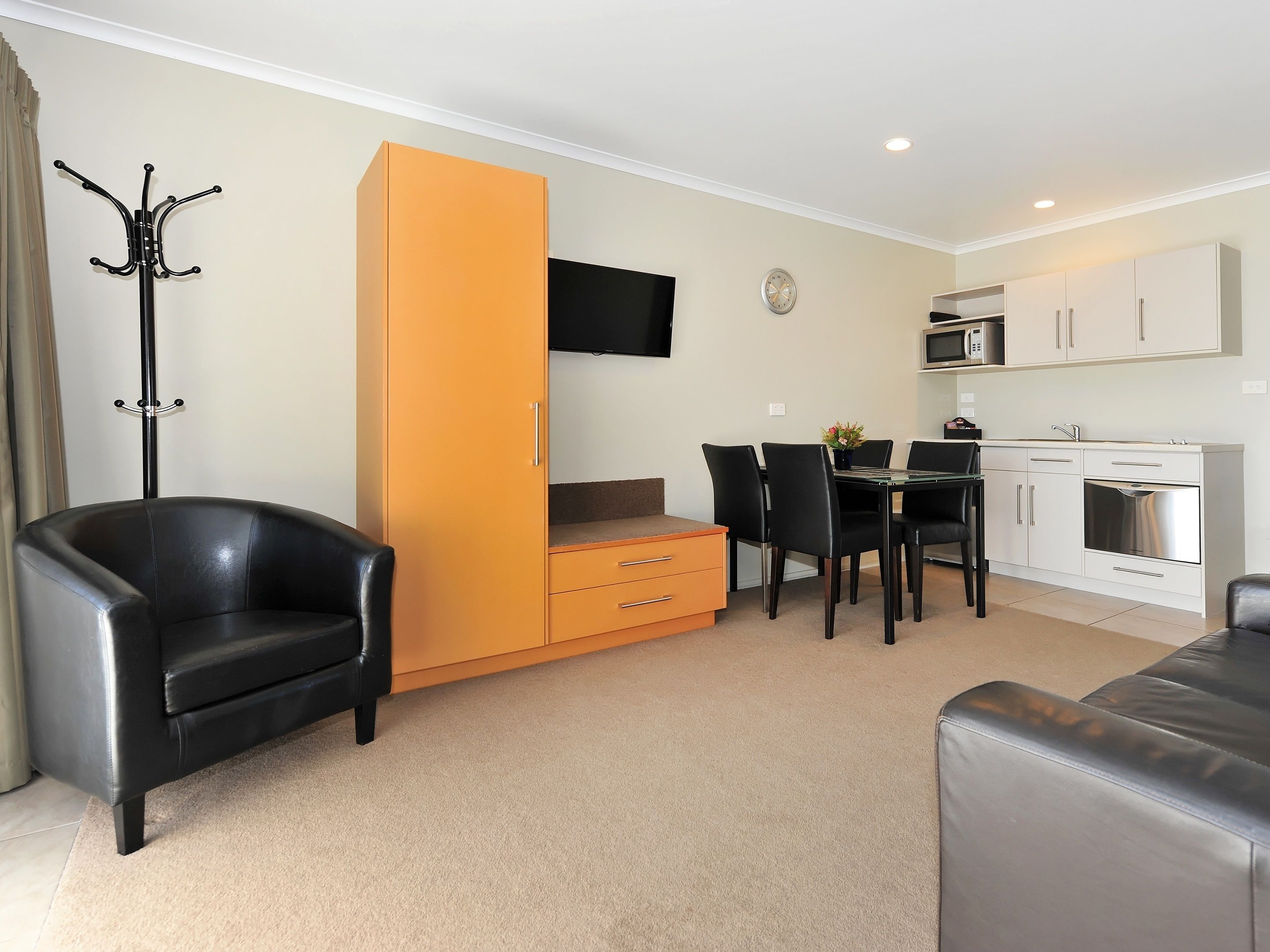 A compact living space with a sofa, a dining table with chairs, a kitchenette, and a coat rack.