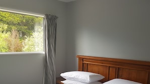 A neatly made bed with white linens and pillows, a wooden headboard, and a window with curtains. - Micro villa (Christchurch)