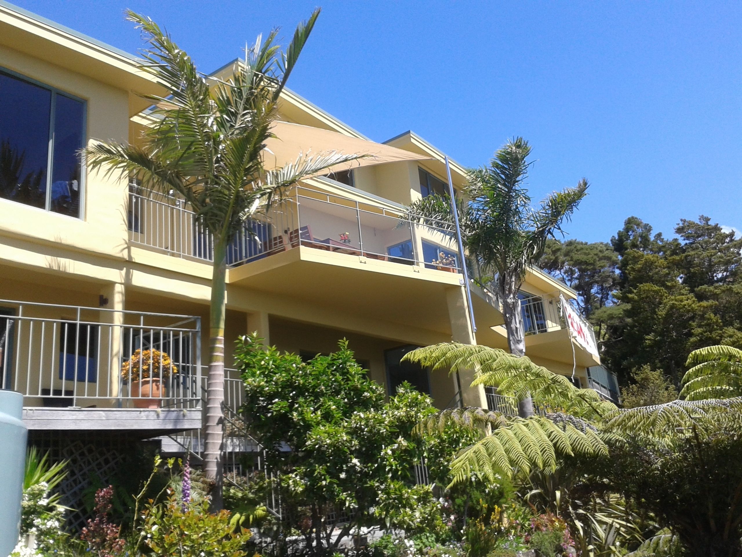 A multi-story building with balconies, surrounded by lush greenery and palm trees.
