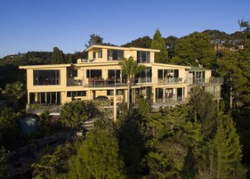 Una casa moderna de dos pisos con ventanas amplias, balcones y un jardín exuberante.