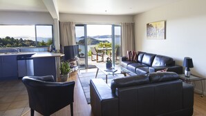 Una sala de estar moderna con un sofá de cuero negro, una zona de comedor con mesa y sillas, y una cocina con lavavajillas.