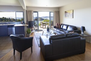 Una sala de estar moderna con un sofá de cuero negro, una zona de comedor con mesa y sillas, y una cocina con lavavajillas.