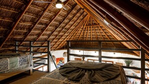 A room with a thatched roof, wooden beams, a bed with patterned bedding, and a hanging light fixture. - Casa Paz (Isla Holbox)