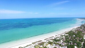 An aerial view of a coastal area with a beach, clear turquoise waters, and a cluster of thatched-roof buildings. - Casa Paz (Isla Holbox)