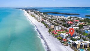 An aerial view of a coastal area with a beach, buildings, and a red location marker.