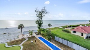 A beachfront property with a pool, a tennis court, and a view of the ocean.