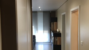 A hallway with a kitchen area, a dining table, and a window with blinds. - Luxury apartment (Apach)