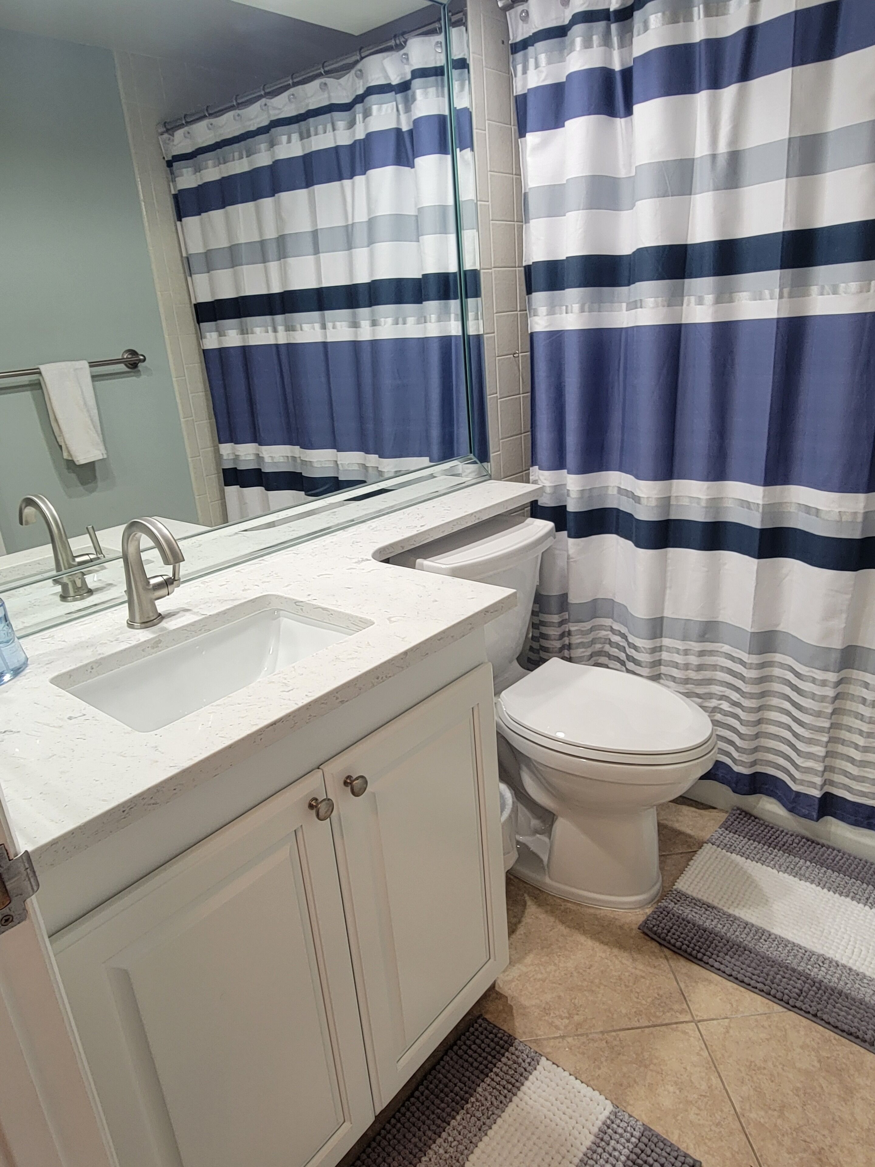 Une salle de bain avec un lavabo blanc, un miroir, des toilettes et un rideau de douche à rayures.