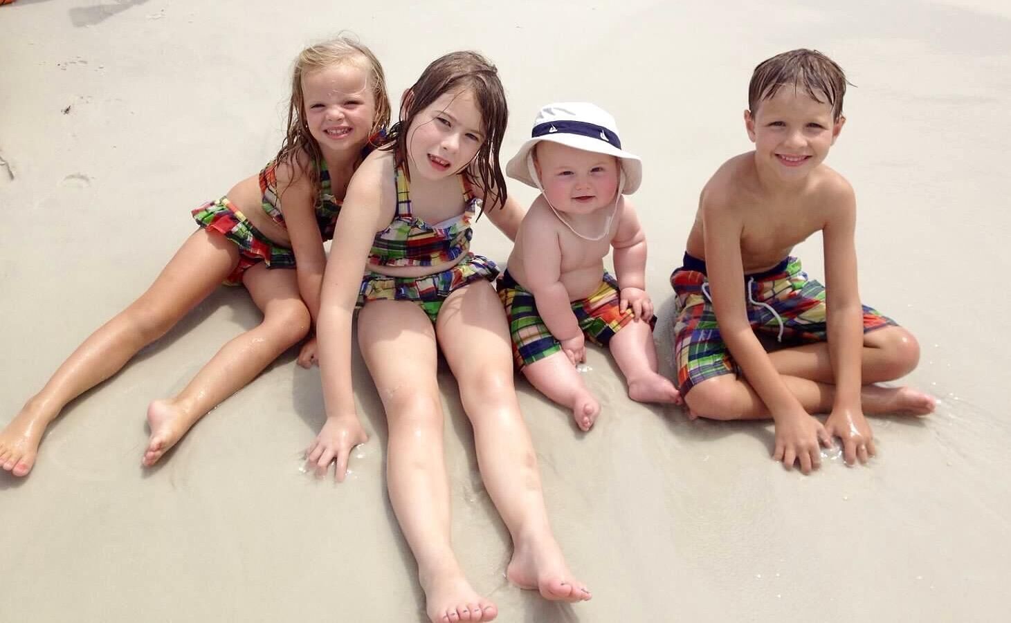 Four children sitting on a sandy beach.