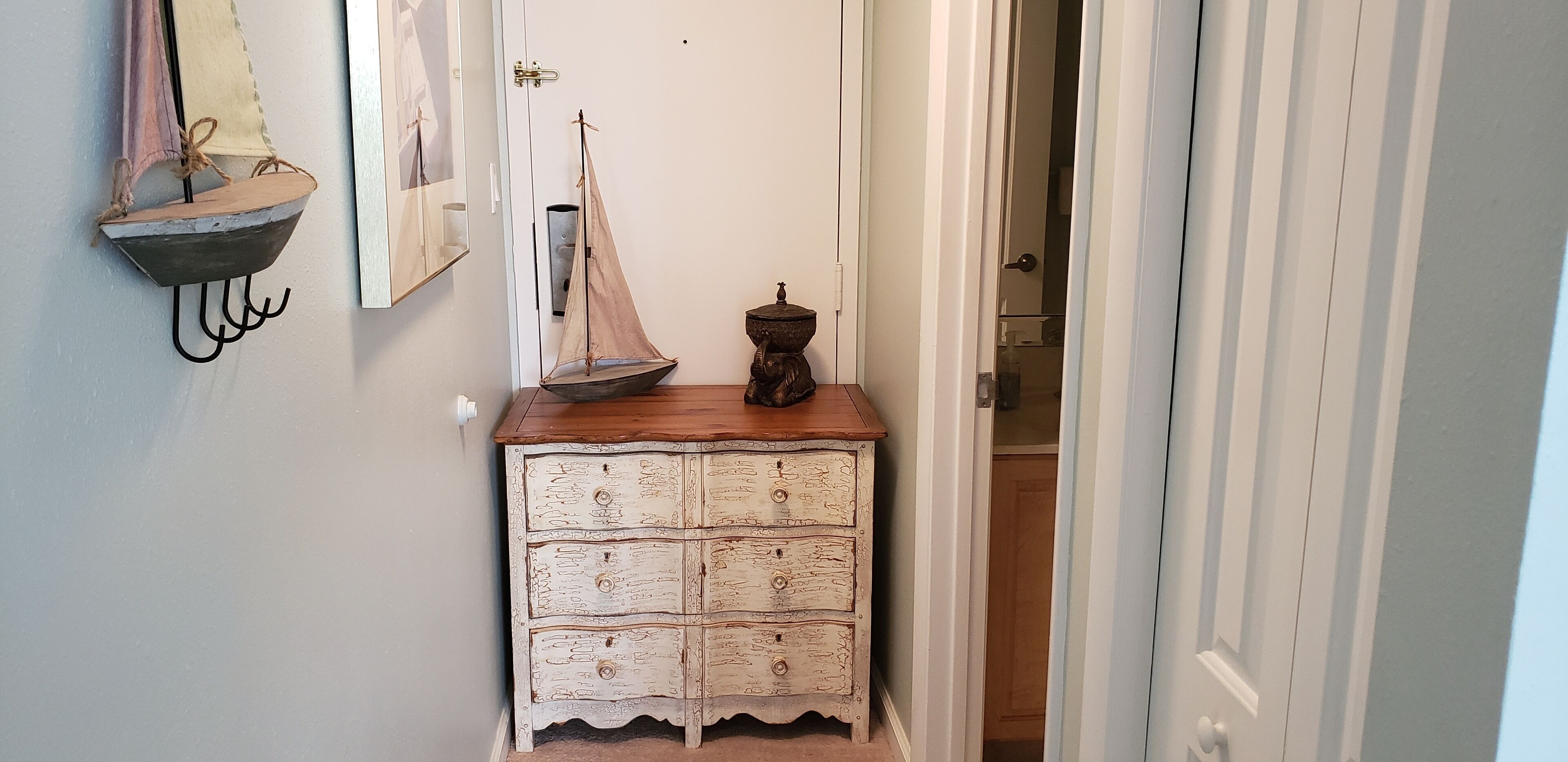 A hallway with a wooden dresser, a small sailboat decoration, and a door leading to another room.