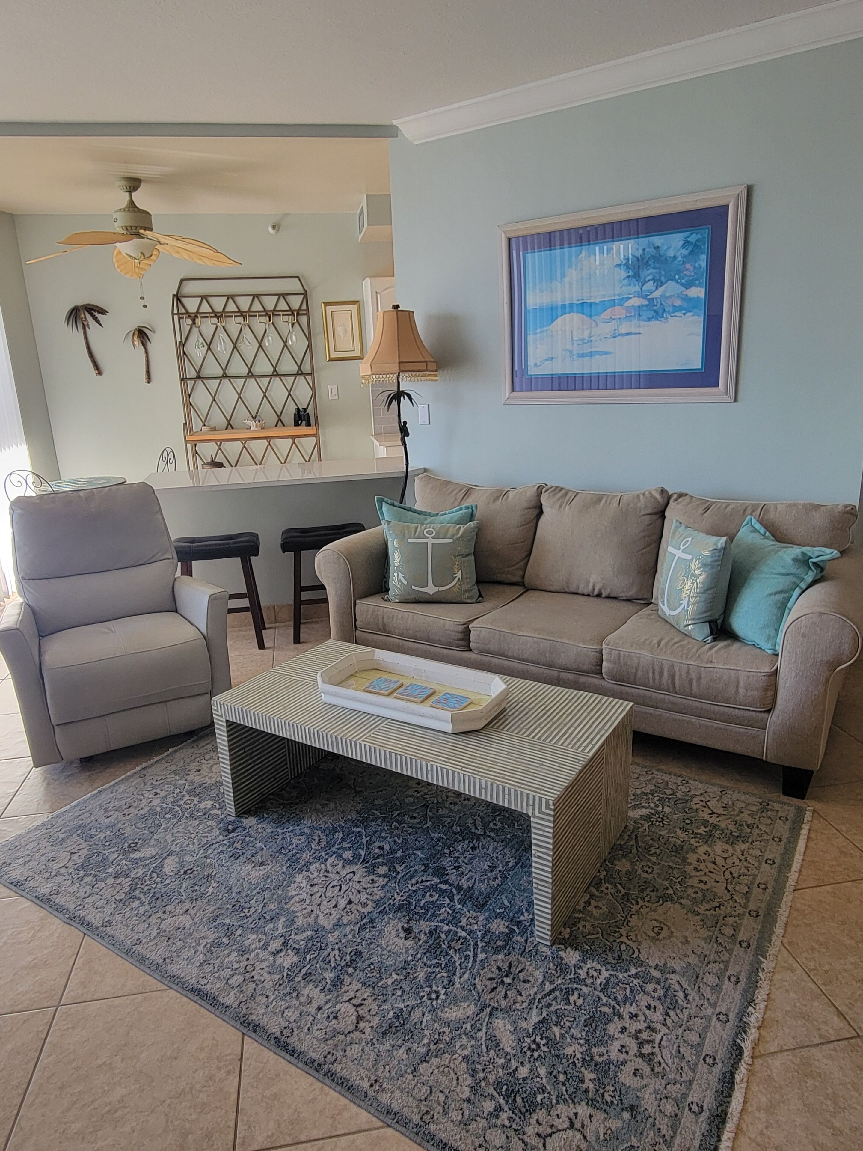 A living room with a beige sofa, a striped coffee table, and a blue patterned rug.