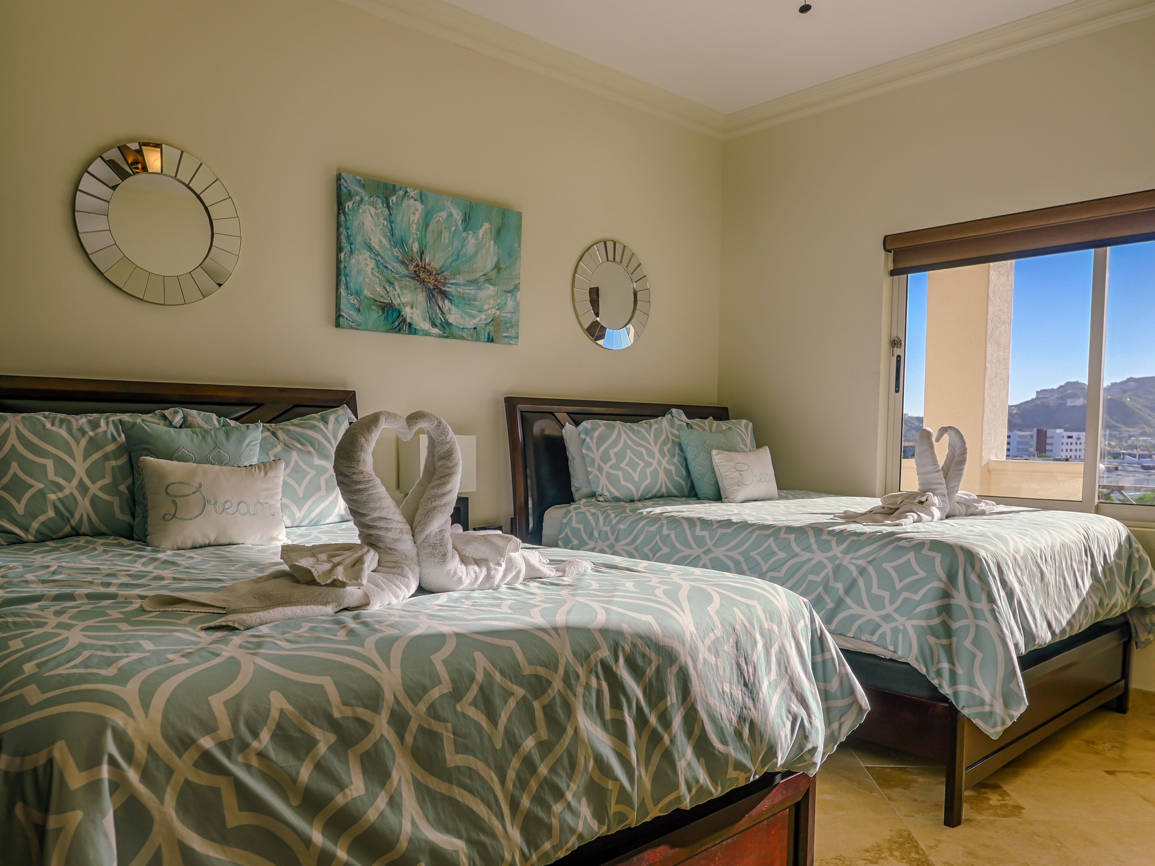 Een hotelkamer met twee bedden, elk voorzien van beddengoed met een patroon en decoratieve kussens. Aan de muur boven de bedden hangen klokken en een schilderij.