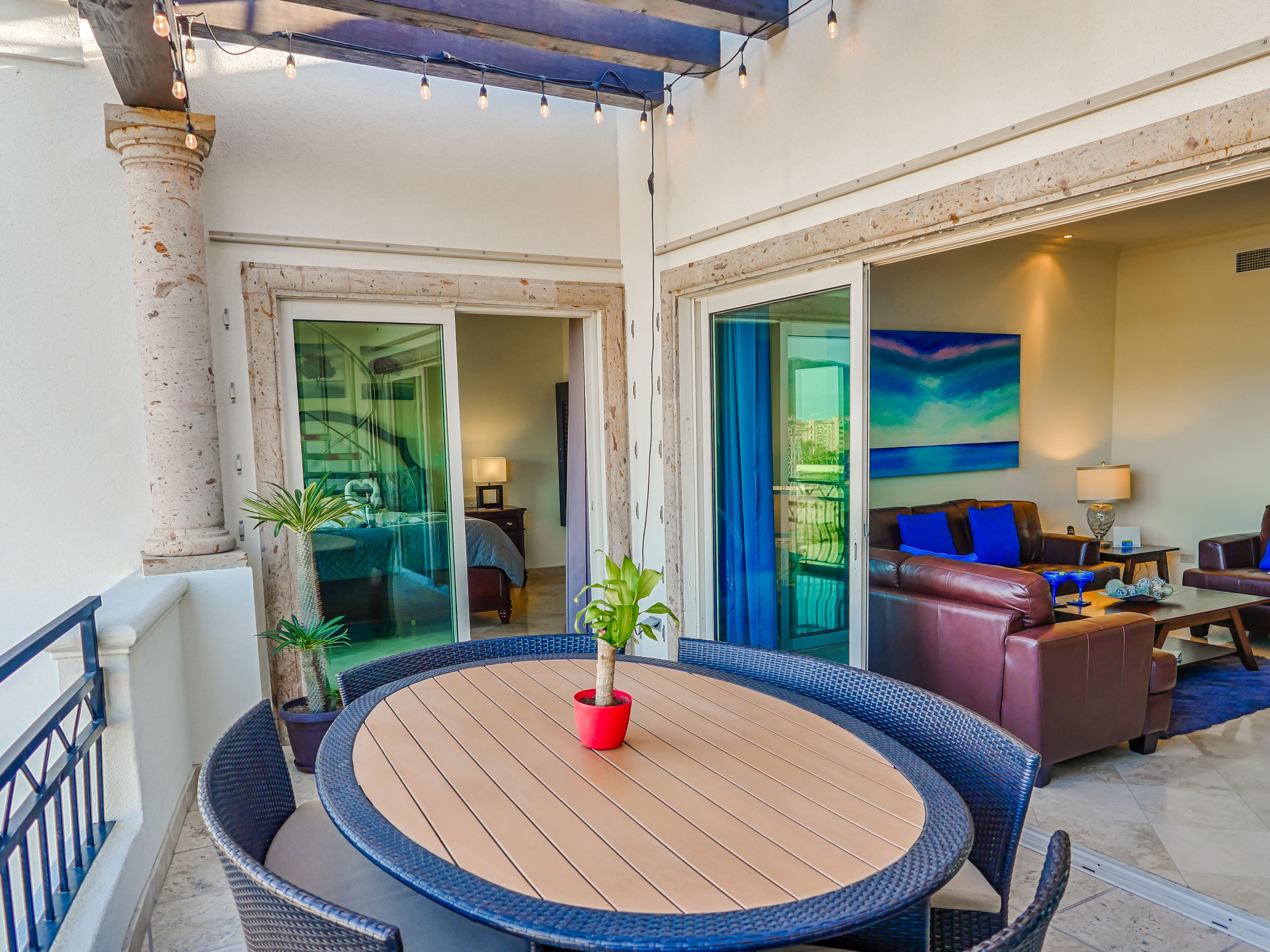 A spacious balcony with a round wooden table, comfortable seating, and a view of the interior.
