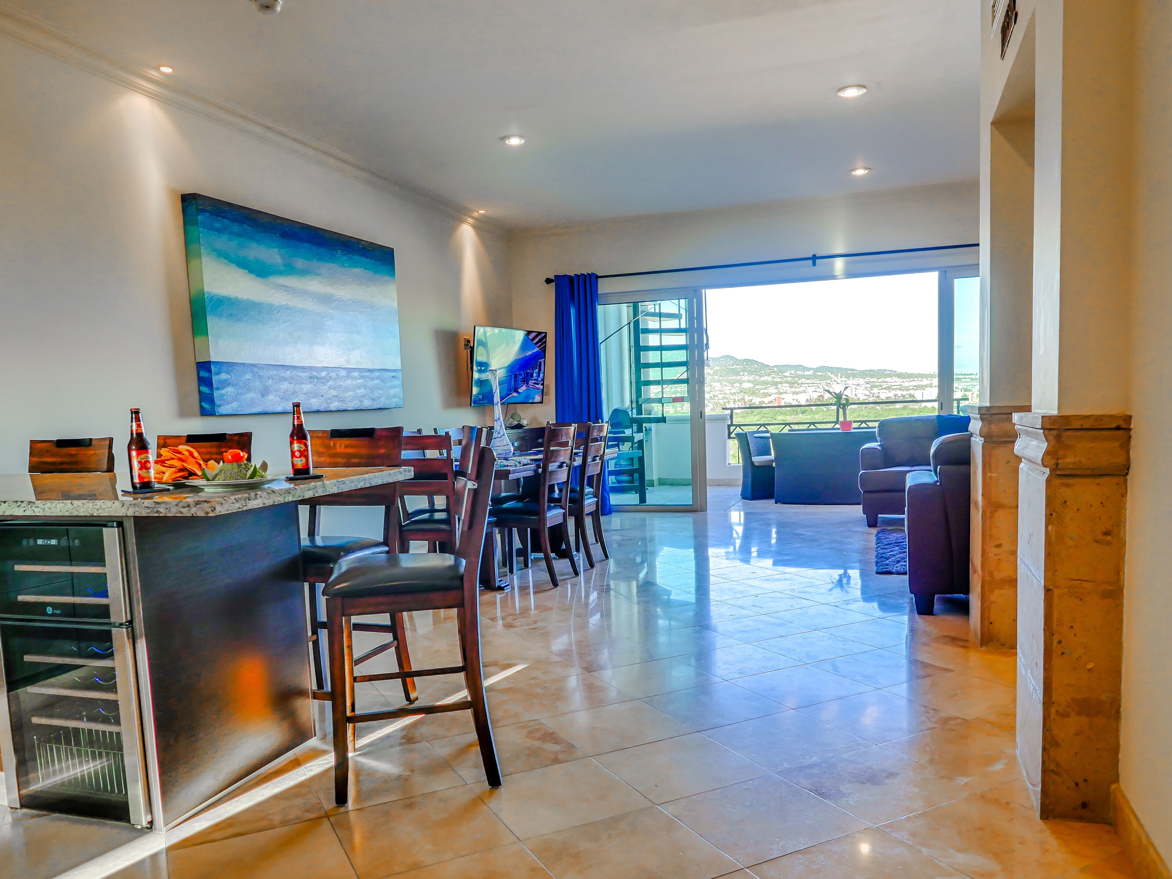 Cocina moderna con una isla grande, comedor con sillas, un sofá y un televisor.