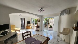 Un amplio espacio habitable con una mesa de comedor, sillas, un televisor y un gran ventanal corredizo que da a un jardín.