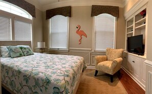 A bedroom with a bed, a chair, a TV, and a wall-mounted shelf.