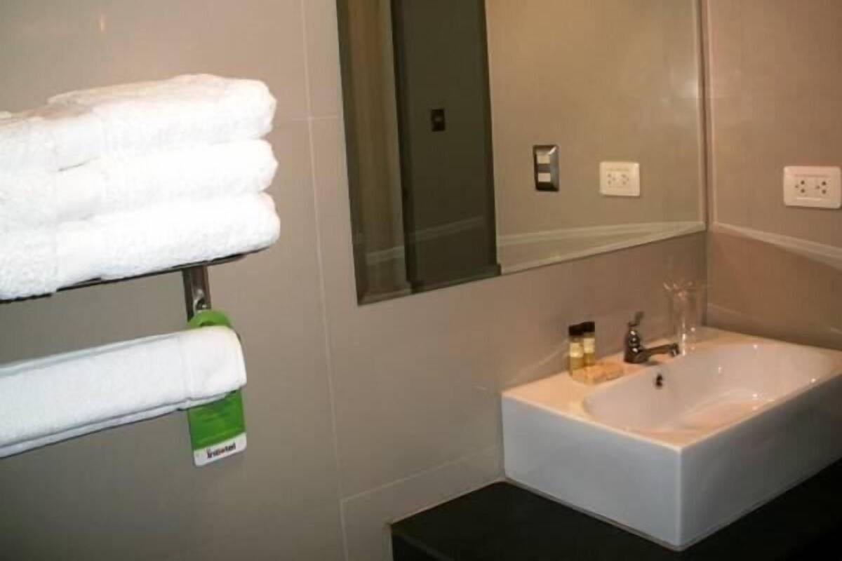 Une salle de bain avec un lavabo blanc, un miroir et un porte-serviettes avec des serviettes blanches.