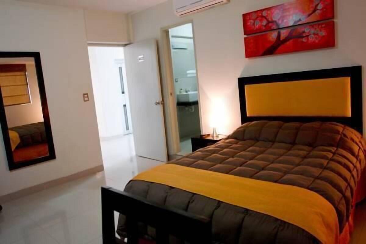 Une chambre à coucher comprenant un lit, une table de chevet, un miroir et une porte donnant sur une salle de bain.