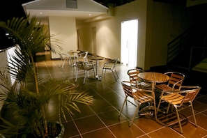 Relax in a stylish indoor space with round tables and comfortable seating, surrounded by lush greenery.