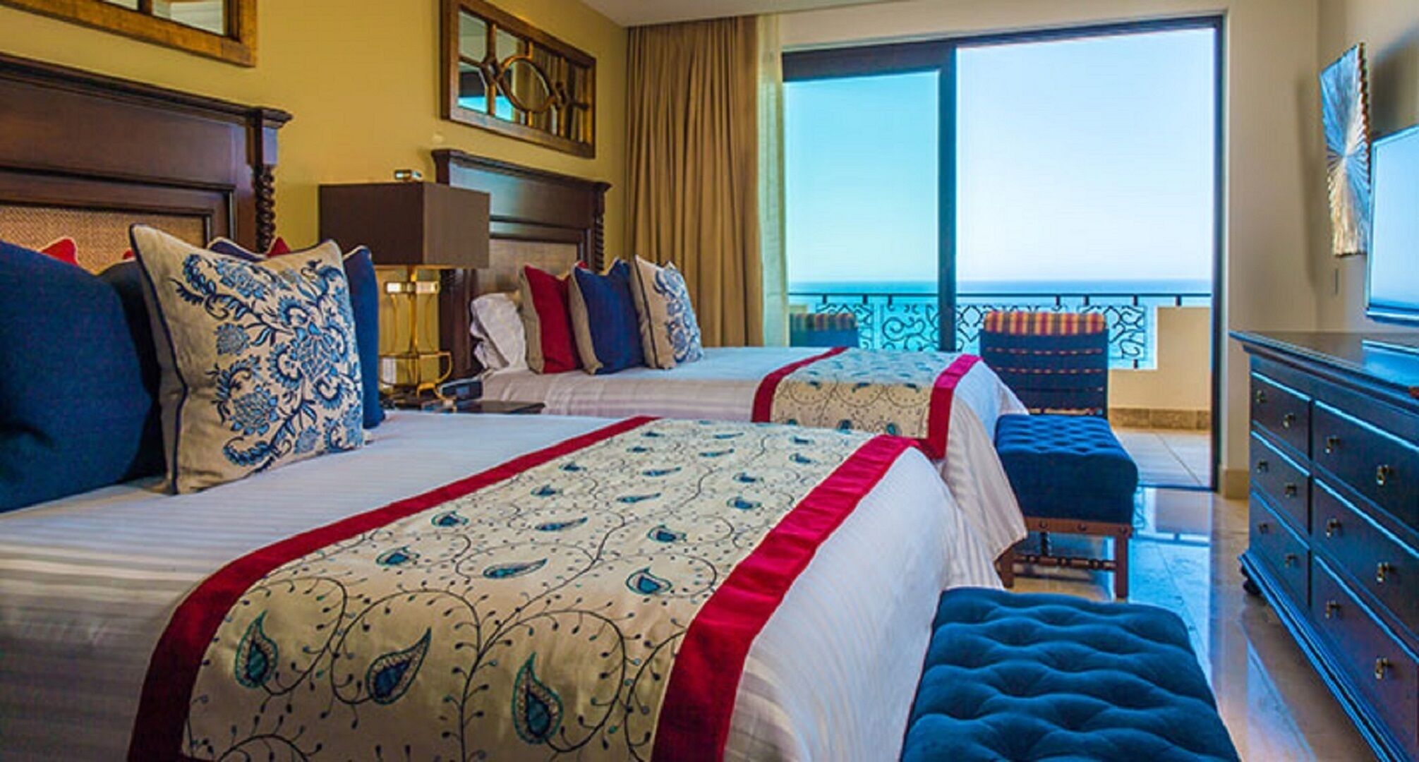 A hotel room with two beds, a balcony, and a view of the ocean.