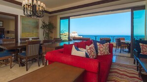 A spacious living area with a red sofa, dining table, and chairs, overlooking a balcony with a view of the sea. - Presidential Suite at Grand Solmar Lands End Resort. Week 52 available! (Cabo San Lucas)
