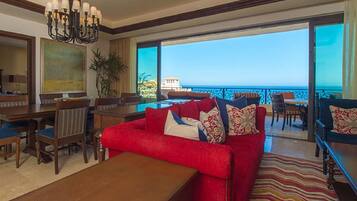 A spacious living area with a red sofa, dining table, and chairs, overlooking a balcony with a view of the sea.