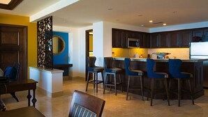 A modern kitchen with dark wooden cabinets, a central island with bar stools, and a blue accent wall. - Presidential Suite at Grand Solmar Lands End Resort. Week 52 available! (Cabo San Lucas)