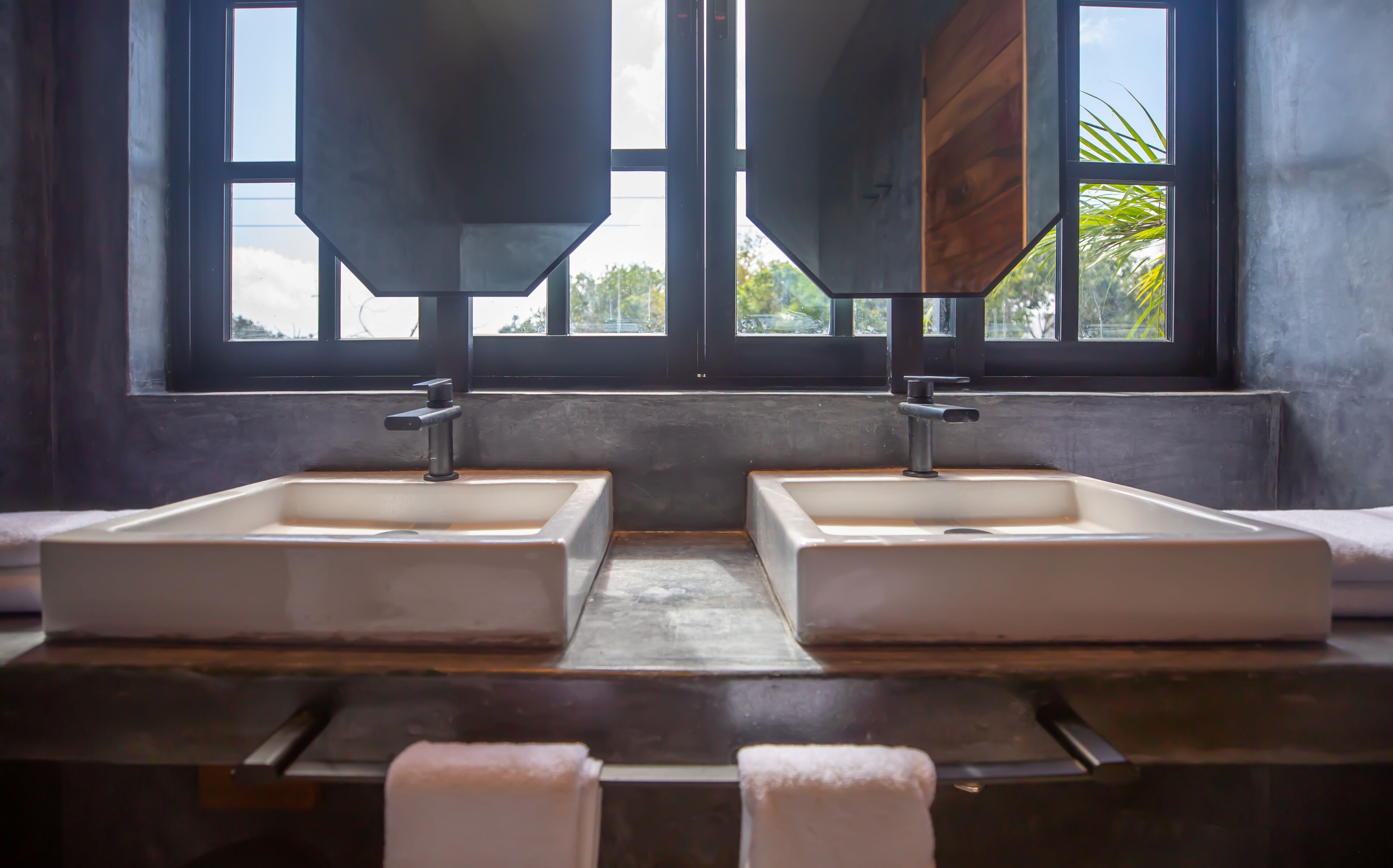 A bathroom with two large sinks, a wooden countertop, and a window with a view of greenery.
