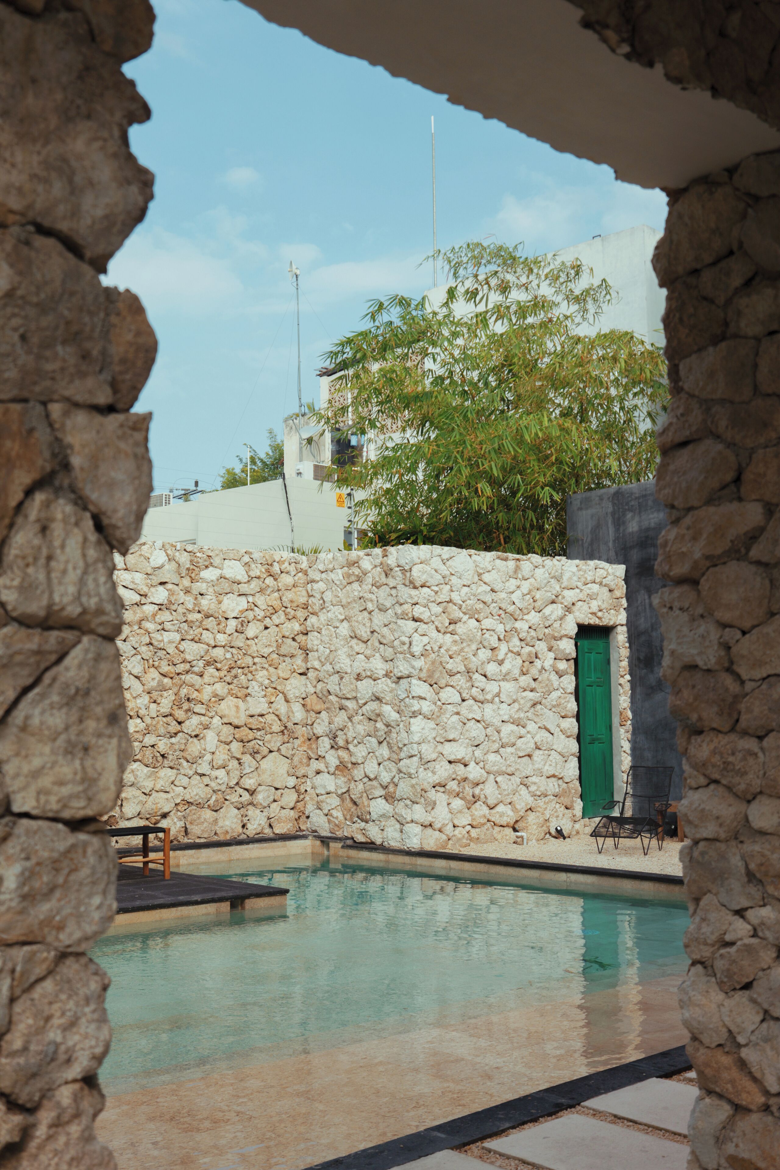 Un mur de pierre avec une porte verte, une piscine et un ciel dégagé.