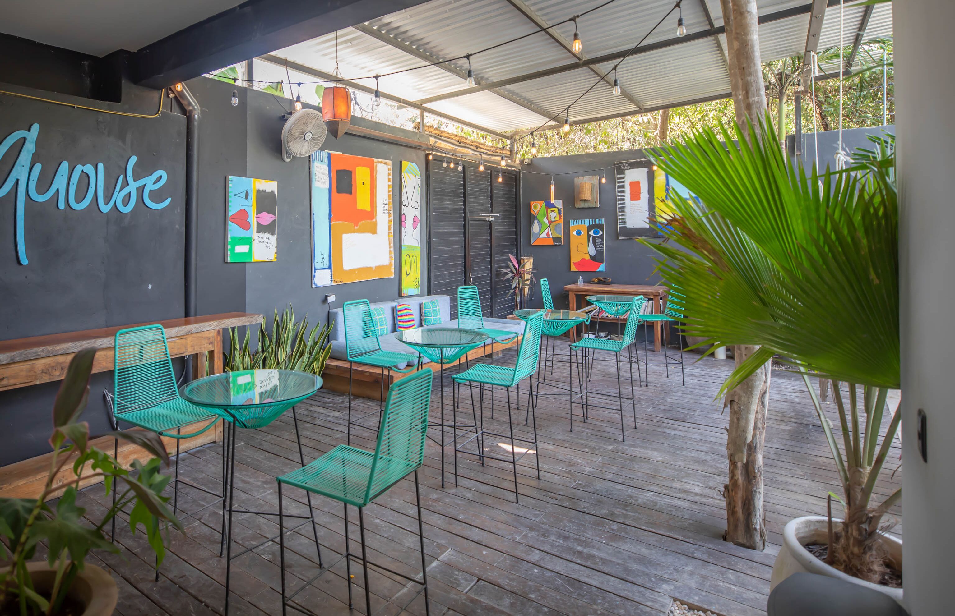 An outdoor patio area with green metal chairs and tables, wooden benches, and potted plants.