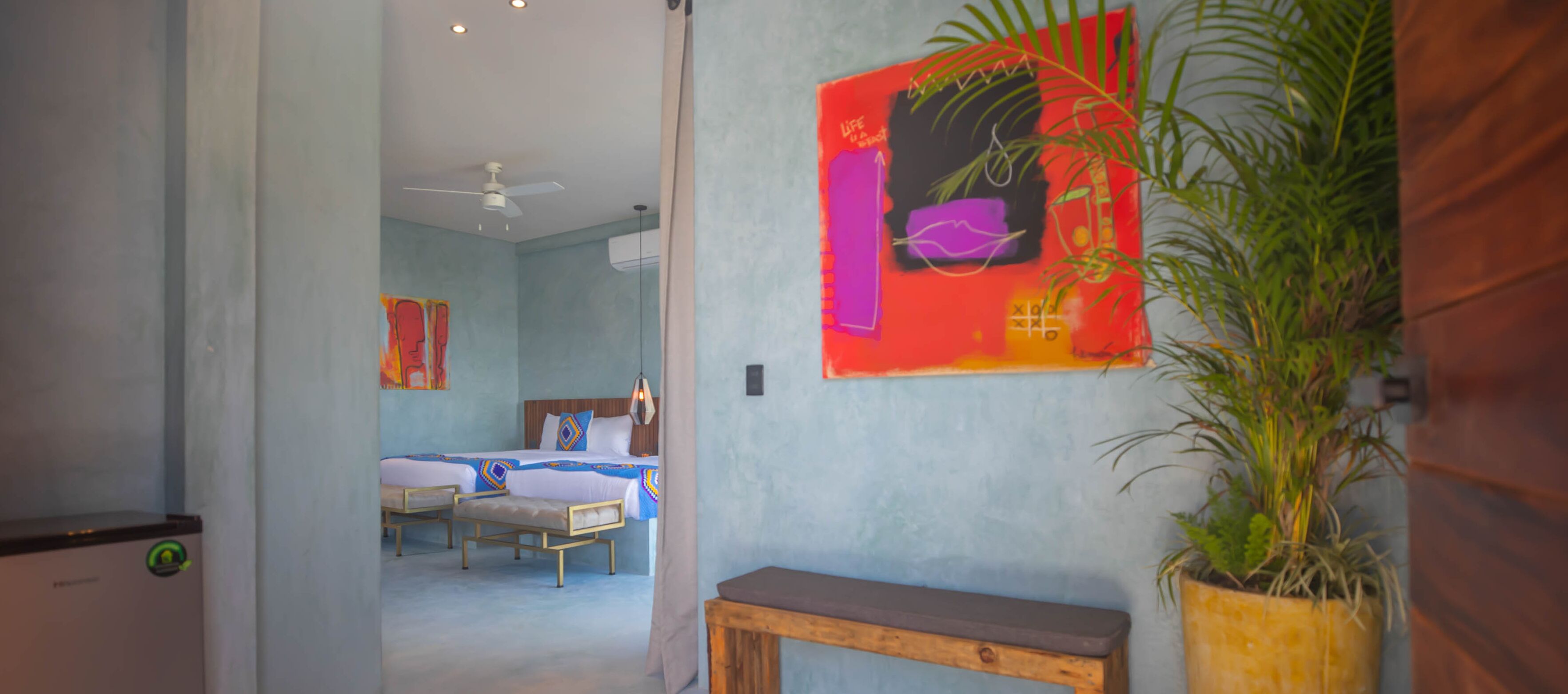 A hotel room with a bed, bedside tables, a bench, and a potted plant.