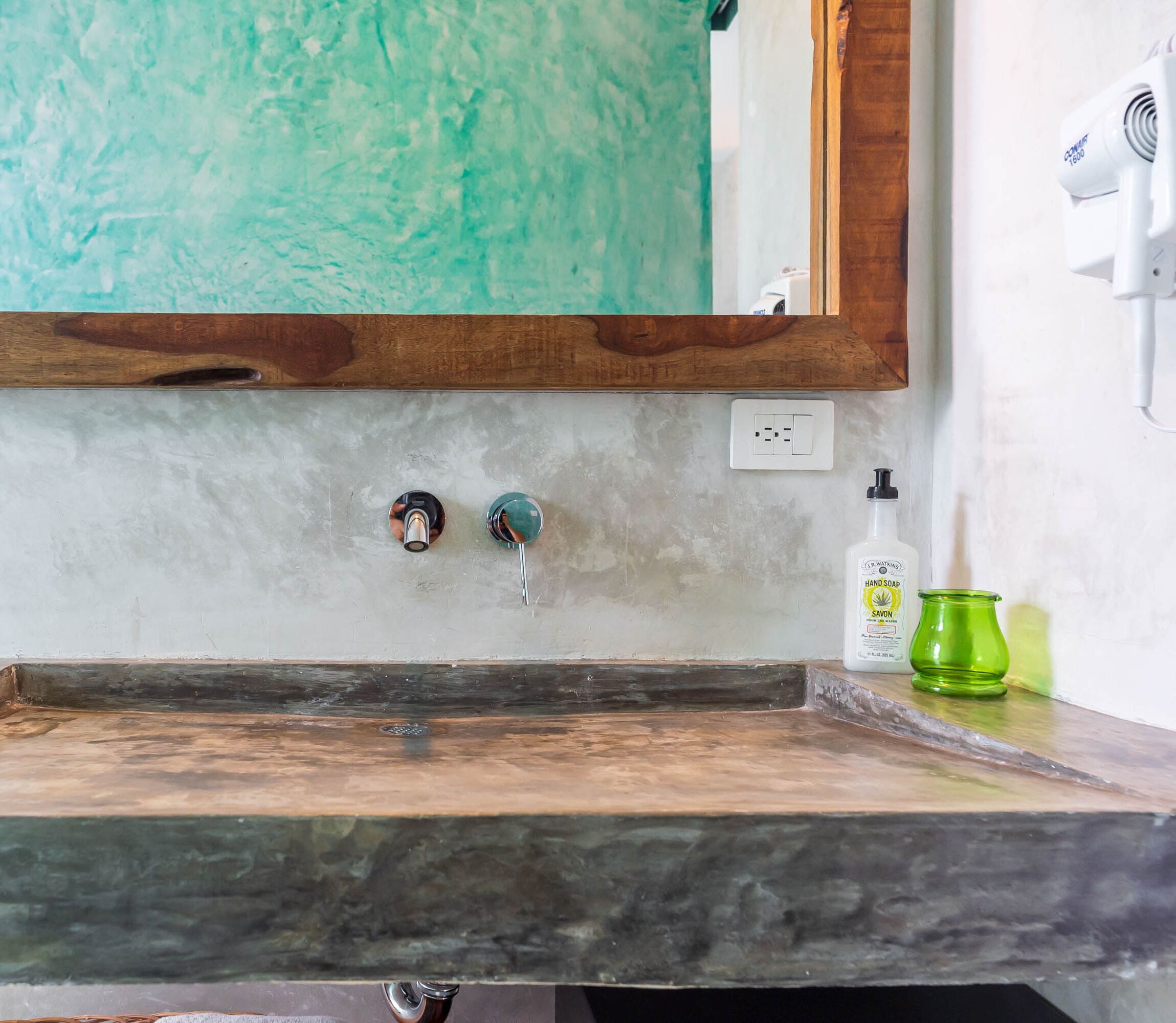 A bathroom with a wooden countertop, a mirror, a faucet, a soap dispenser, and a green glass.