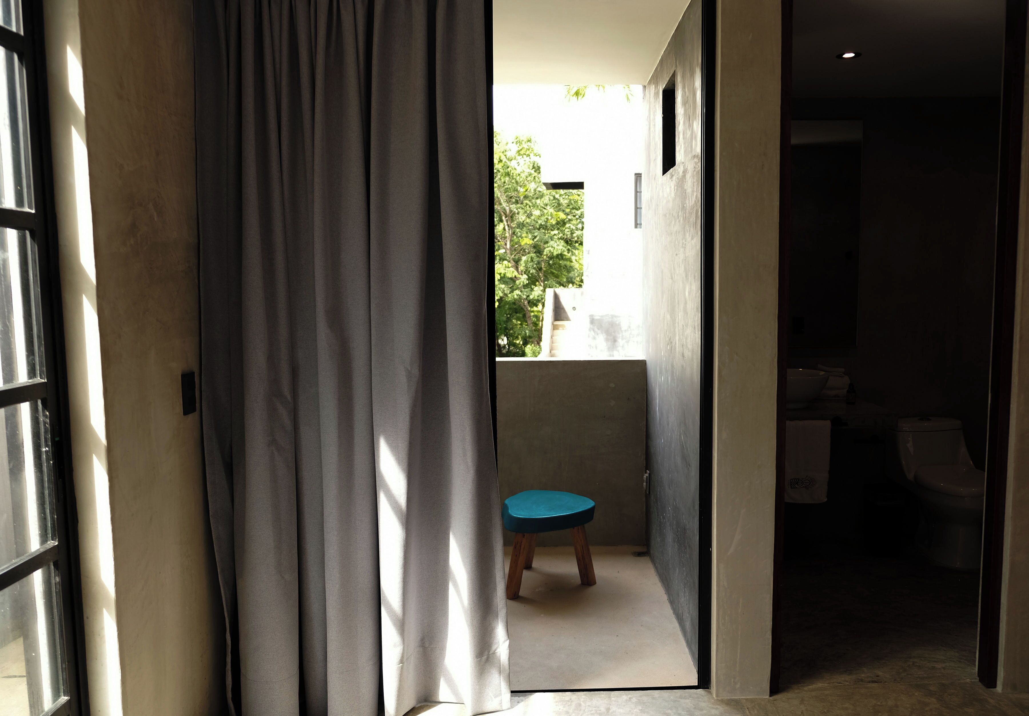 A narrow hallway with a small stool in the center, leading to a bathroom with a toilet and sink.
