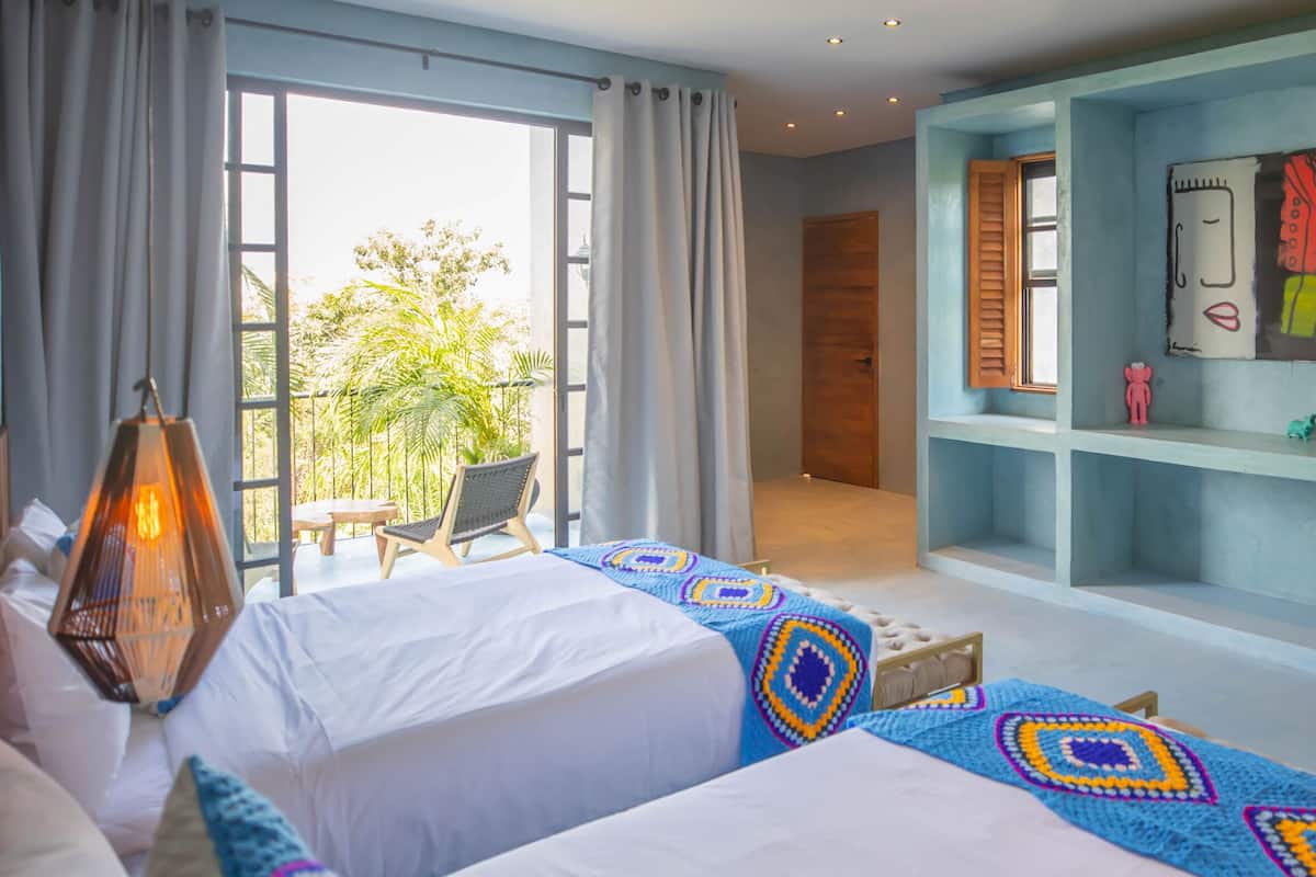 A bedroom with a large bed, a view of the outdoors, a wooden headboard, and a wall with shelves.