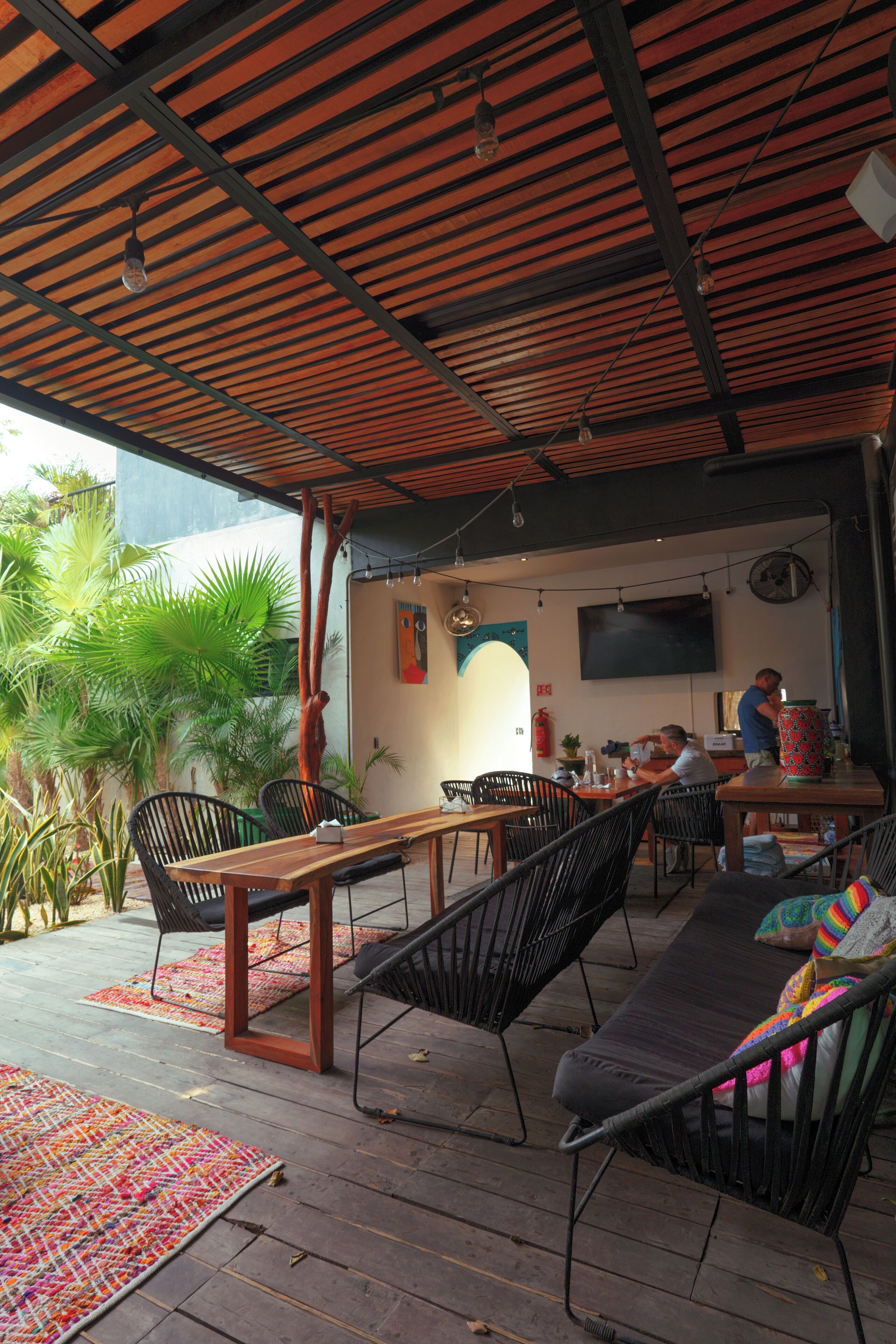 An outdoor seating area with wooden tables and chairs, a TV mounted on the wall, and a fire extinguisher.