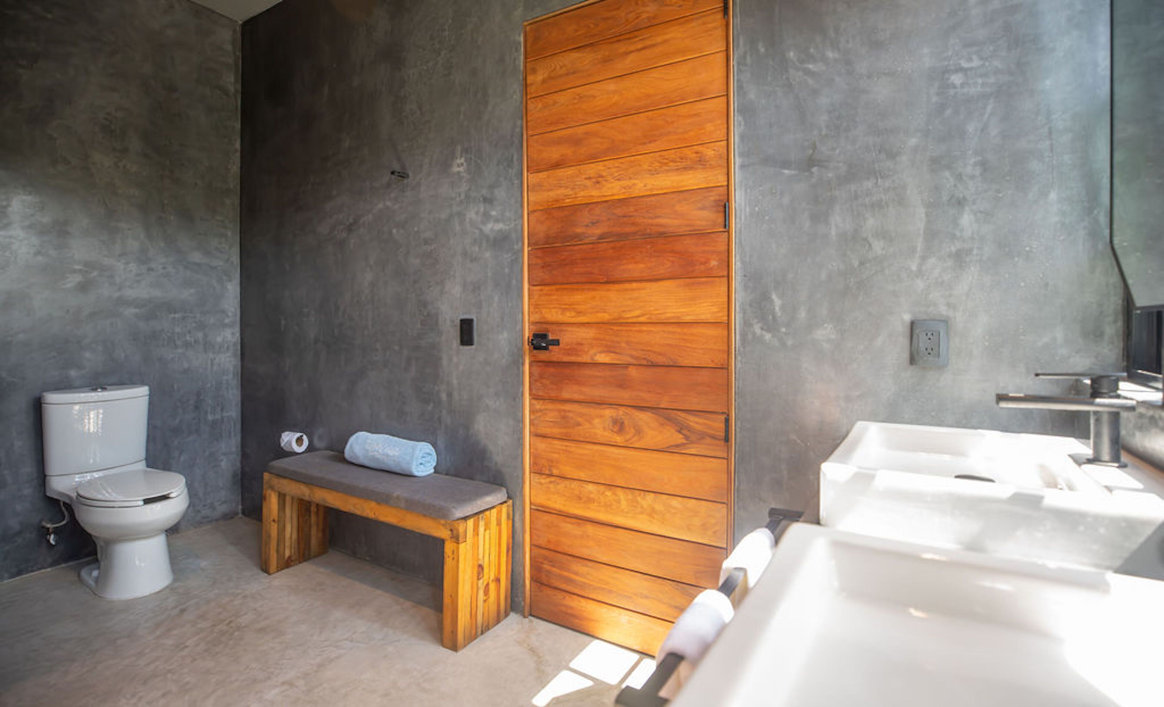 Un bagno con porta in legno, un water, una panca e un lavandino.