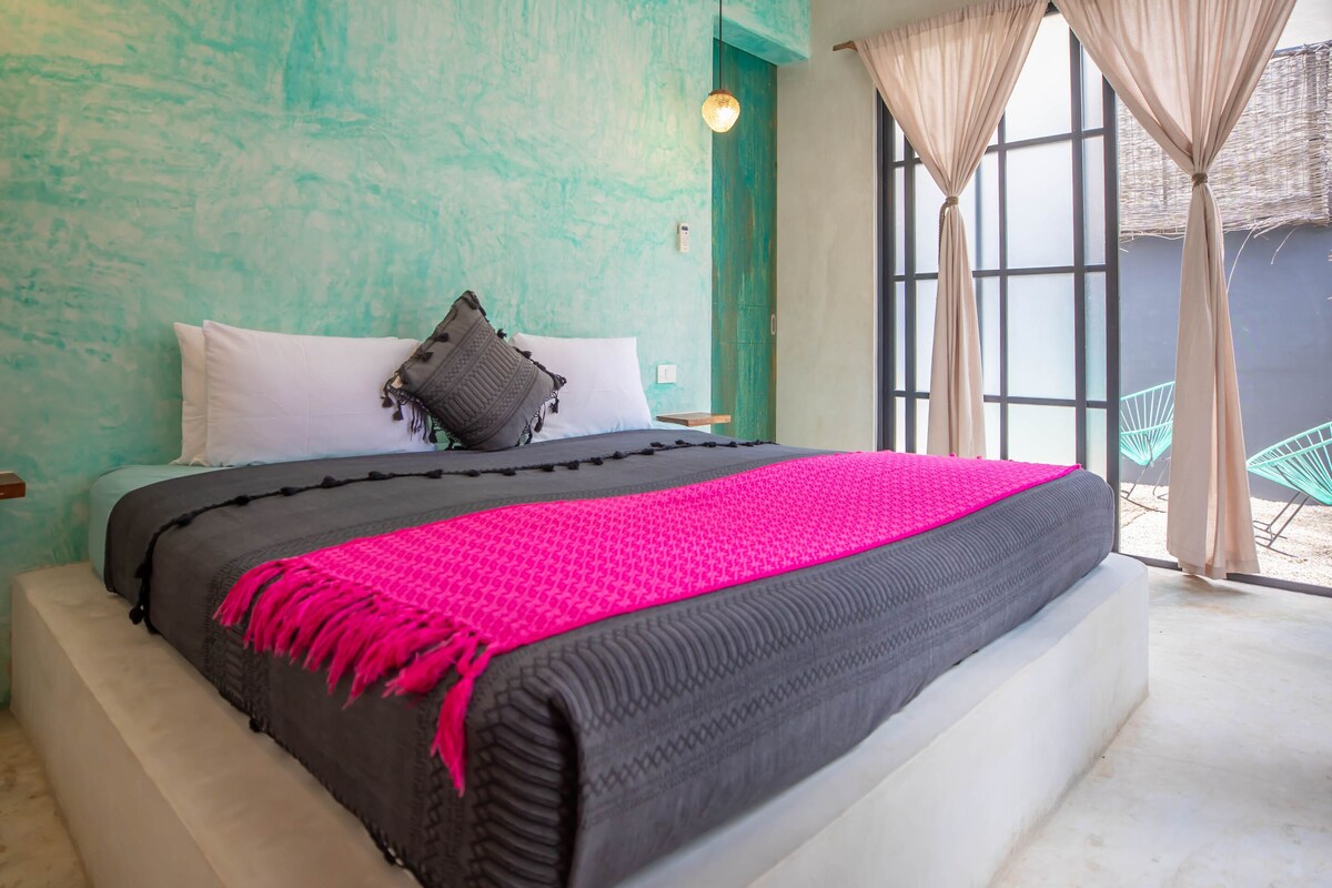 A bed with a black and pink blanket, white pillows, and a teal wall.