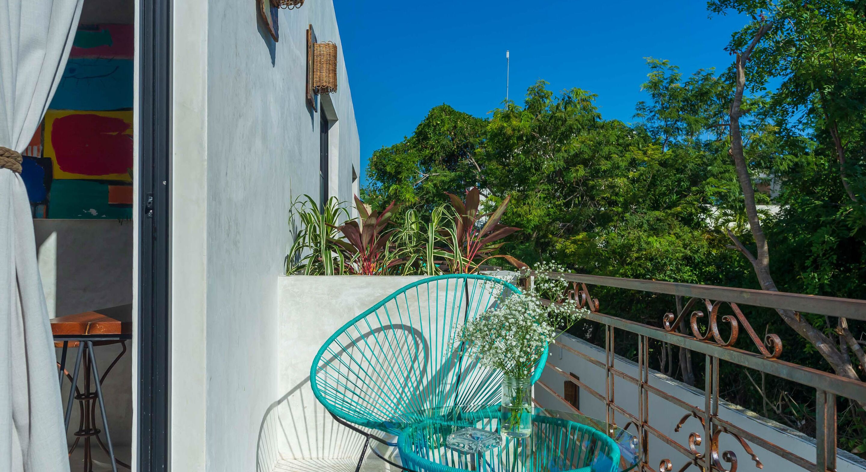 Un balcon avec une chaise turquoise, une petite table et une balustrade blanche.