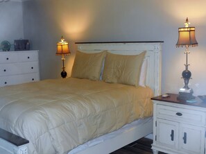 A bed with a beige quilt, two bedside lamps, a white dresser, and a nightstand with a lamp.