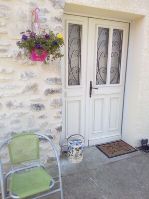 A white door with decorative glass panels, a stone wall, a green chair, a metal bucket, and a doormat.