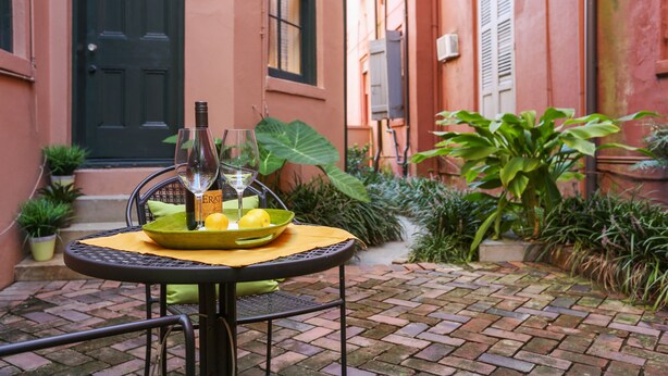 Une terrasse avec une table ronde, une bouteille, un verre et un saladier de fruits.