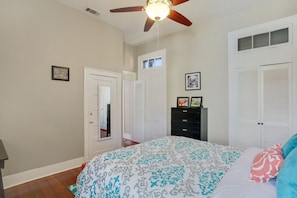 A bedroom with a ceiling fan, a bed with patterned bedding, a dresser, and a door leading to another room. - Upscale, Modern Apartment on Bourbon St with Balcony overlooking Courtyard (New Orleans)