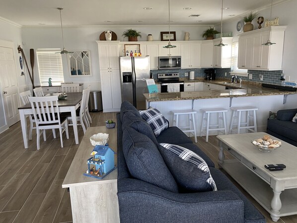 A modern kitchen with white cabinets, a central island with stools, and a dining area with a wooden table and chairs.