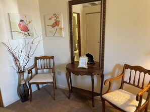 Ein Zimmer mit zwei Holzstühlen, einem kleinen Tisch, einem Spiegel und zwei an der Wand befestigten Bildern von Vögeln.