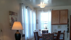 A living room with a sofa, a wooden coffee table with a tray, a lamp, and a dining area with chairs and a table. - The Garden Suite has beautiful views of forests and pastures! It is dog friendly (Ferndale)