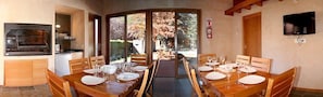 A dining area with a long table set for four, a built-in grill, and a television on the wall.