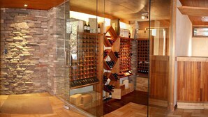 Une cave à vin aux murs de pierre, aux étagères en bois et aux portes en verre.