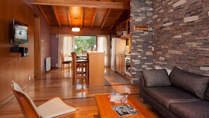 Un salon chaleureux avec un plafond en bois, un mur en pierre, un canapé, une table basse et un téléviseur fixé au mur.