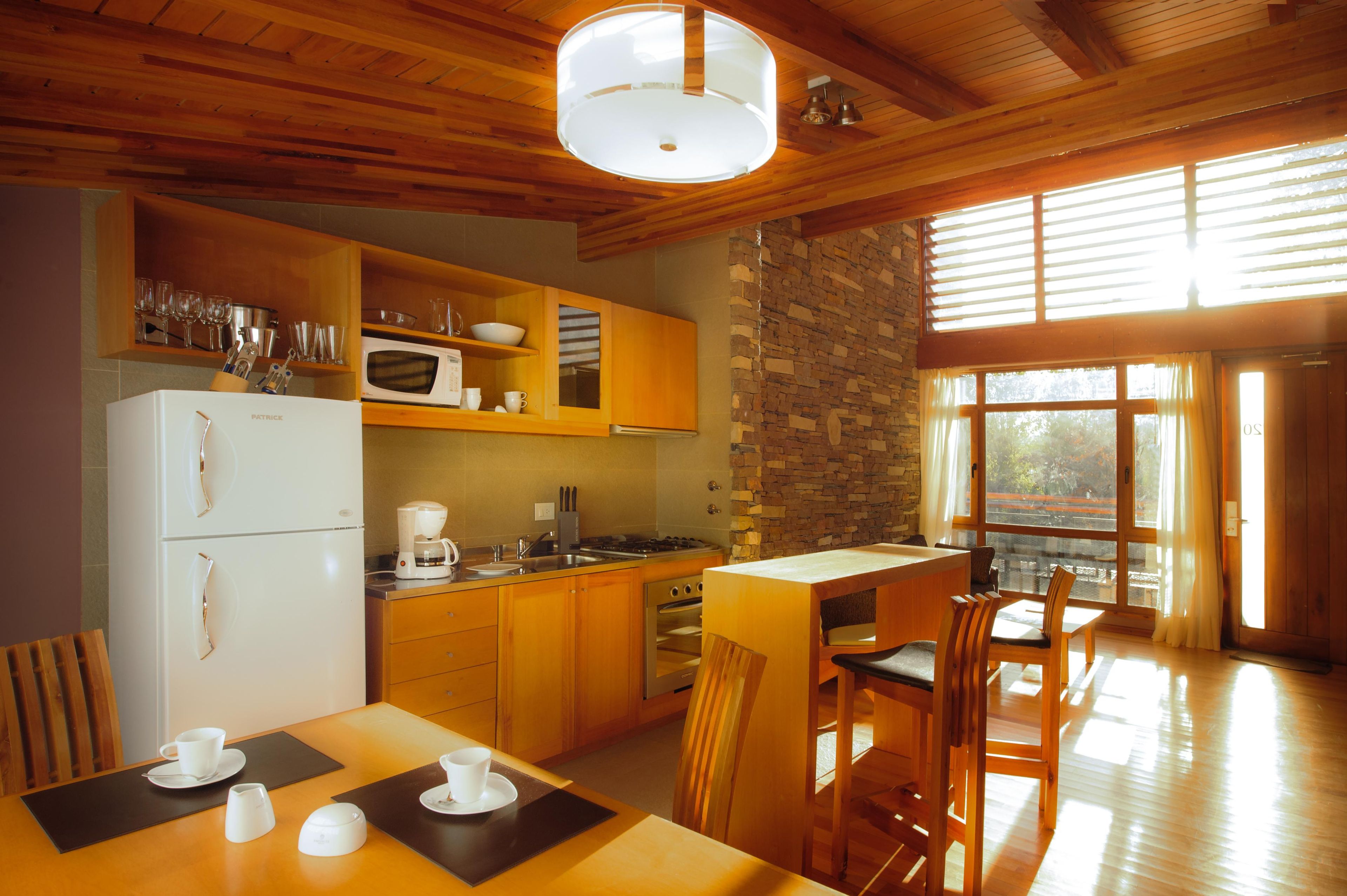 Una cocina con armarios de madera, un refrigerador, un microondas y un comedor con mesa y sillas.